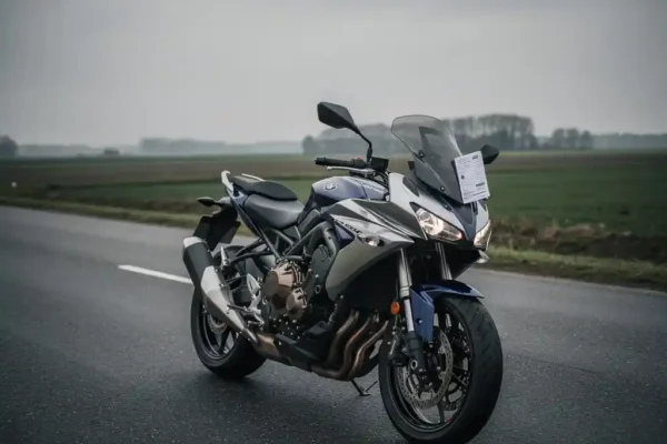 Glanzende motorfiets op Nederlandse weg met verzekeringsdocument onder de windscherm, bewolkte lucht op de achtergrond.