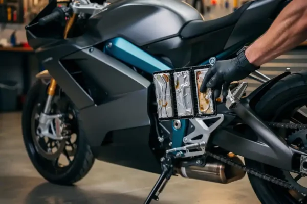 Monteur inspecteert beschadigd lithium-accupakket in elektrische motorfiets in moderne garage met amberkleurig werklicht.