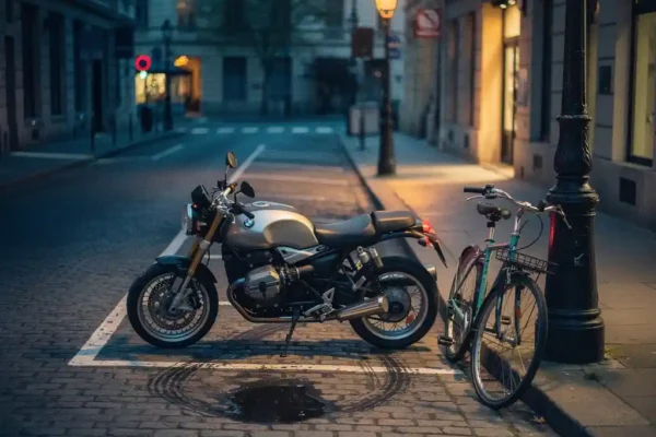 Eenzame motorfiets op een verlaten kinderkopjesstraat bij schemering, met een leeg parkeervak en een huurfietst tegen een lantaarnpaal.