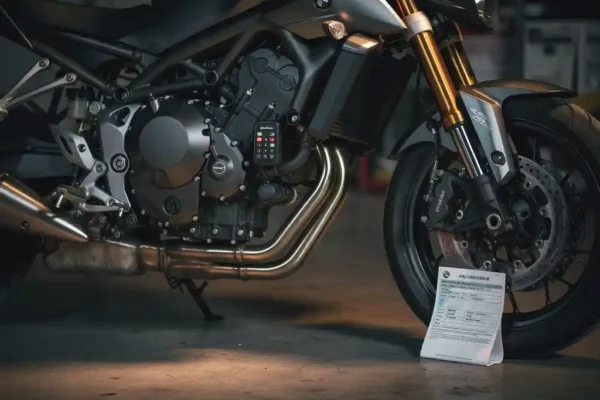 Motorfiets in donkere garage met zichtbaar alarmsysteem op frame en opgevouwen verzekeringsdocument tegen voorwiel.