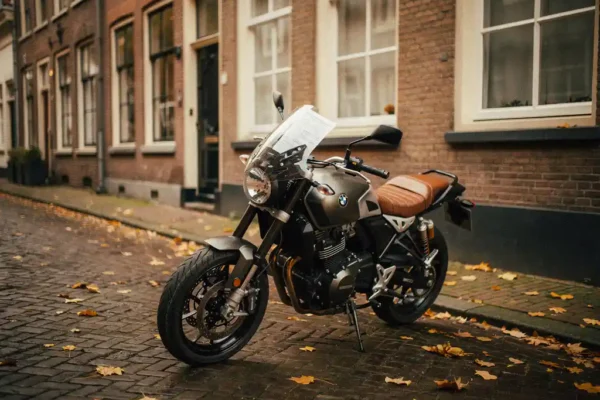Motorfiets geparkeerd op een Hollandse kasseienstraat naast bakstenen gebouw, papieren document onder windscherm, herfstbladeren op de grond.
