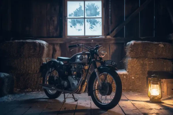 Klassieke motor in verlichte houten schuur, verzekeringsdocument op de tank, vorst op het raam op de achtergrond.