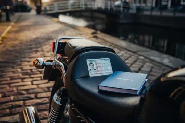 Motorfiets op Amsterdamse straatkeien met buitenlands rijbewijs en Nederlandse verzekeringsdocumenten op het zadel.